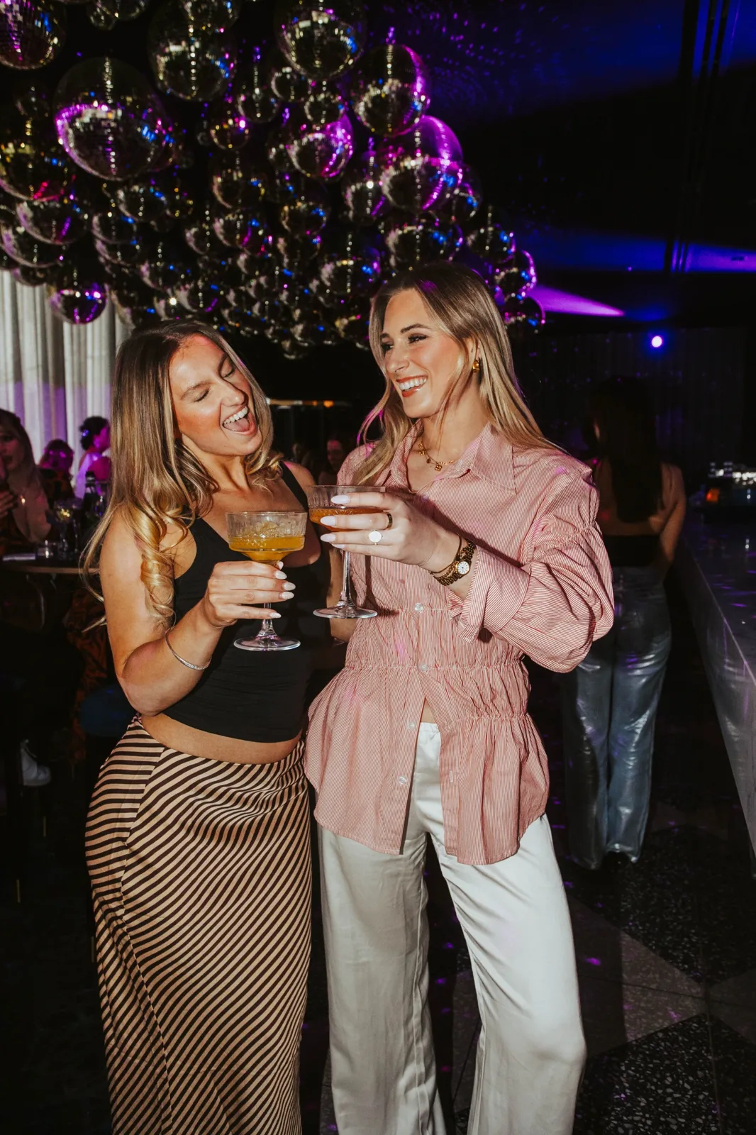Two guests laughing with cocktails under the mirror balls